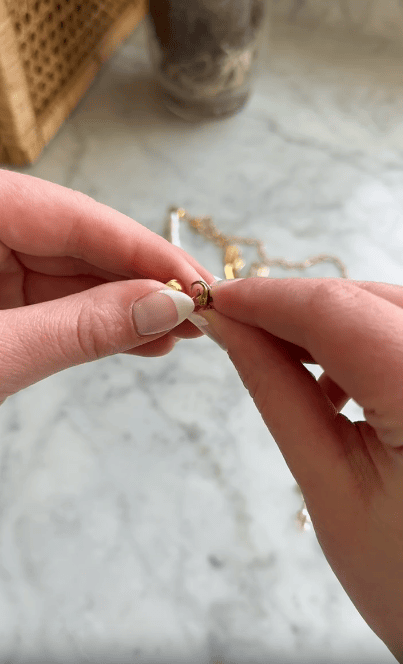 Close-up of hands holding a small gold jump ring with a chain in the background on a marble surface.