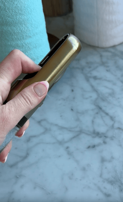 A hand holding a gold and black lighter over a marble countertop. Blue and white cylindrical objects are blurred in the background.
