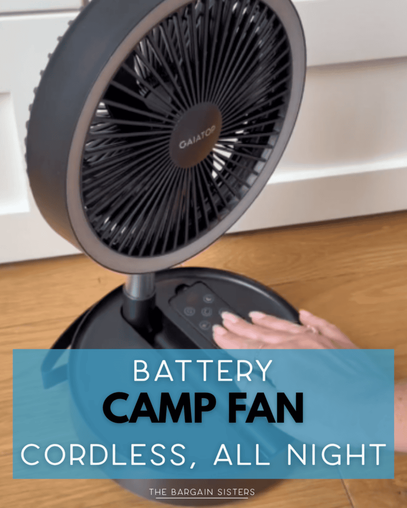 A person adjusting the controls on a black GAITOP battery-powered camp fan placed on a wooden floor. Text overlay reads: "Battery Camp Fan. Cordless, All Night.