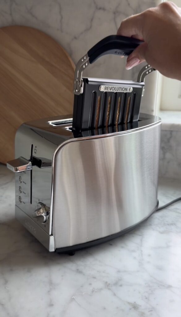 A hand places a cassette tape labeled "REVOLUTION" into the slot of a gleaming Revolution toaster on a marble countertop.