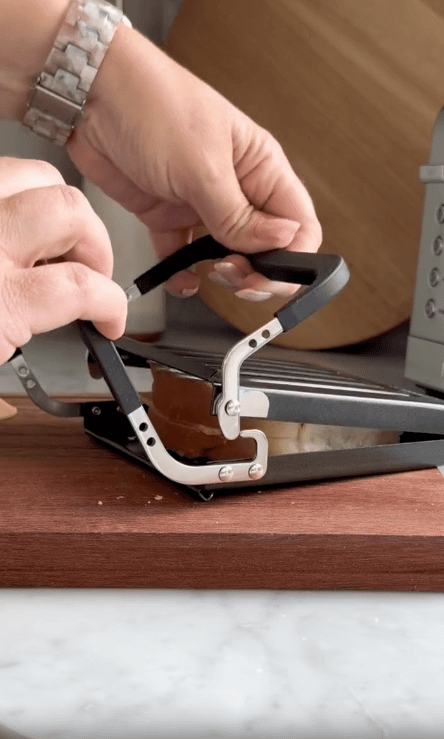 A person presses a toasted sandwich in a Revolution Toastie Press on a wooden cutting board, revealing melted cheese inside.