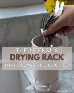 A hand places forks into a white vertical utensil drying rack on a kitchen counter with yellow flowers and marble backsplash in the background. Text overlay reads: "The utensils drying rack that clears the counter.