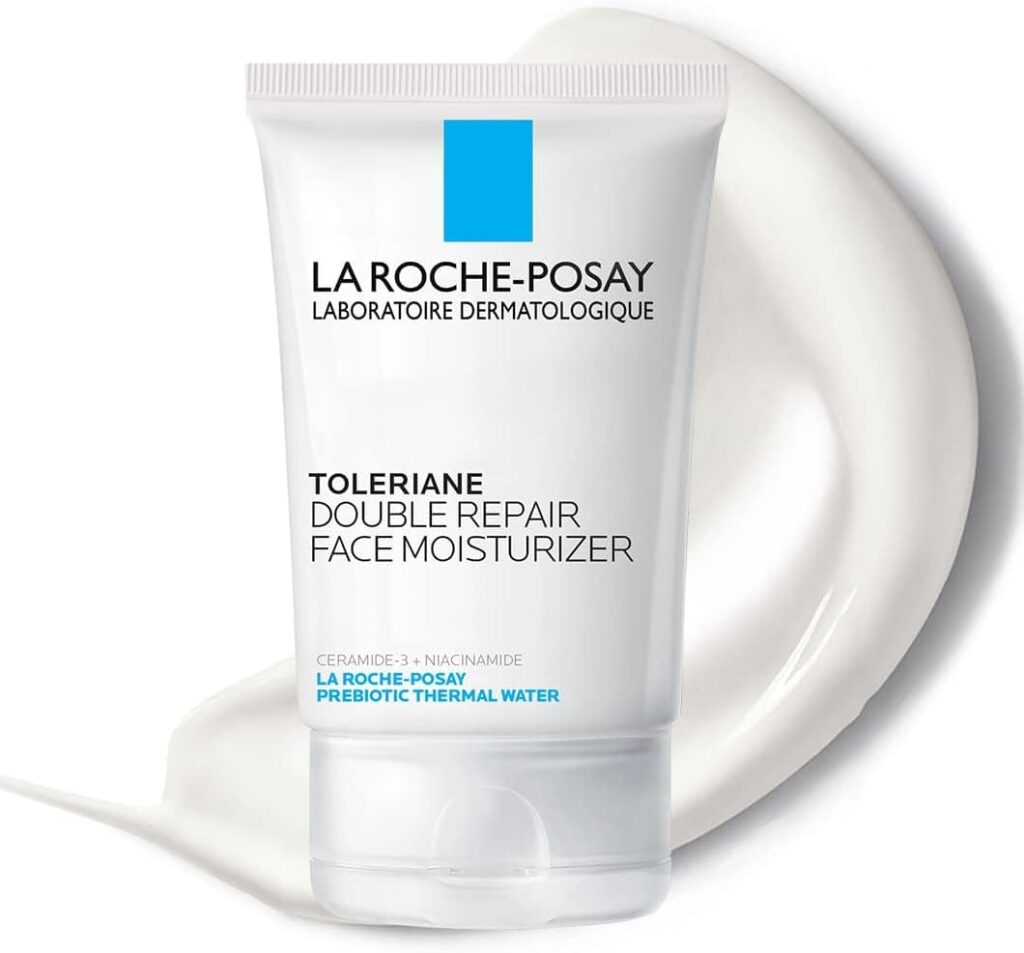 A tube of La Roche-Posay Toleriane Double Repair Face Moisturizer stands upright on a white creamy smear, with product information and blue accents visible on the packaging.