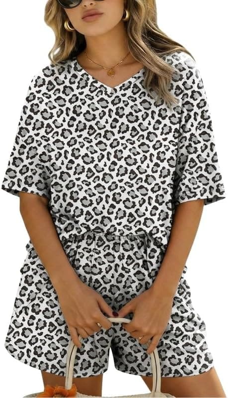 Woman wearing a short-sleeve, V-neck, leopard print matching top and shorts set, holding a bag. She has wavy hair, sunglasses, hoop earrings, and a necklace—perfectly styled for the latest Monday Deals.