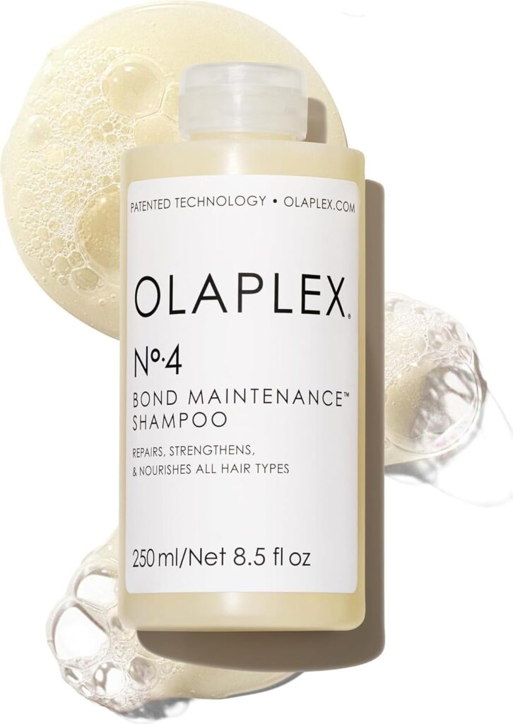 A bottle of Olaplex No. 4 Bond Maintenance Shampoo, 250 ml/8.5 fl oz, stands upright with shampoo bubbles and liquid surrounding it on a white background. The label details its purpose and website.