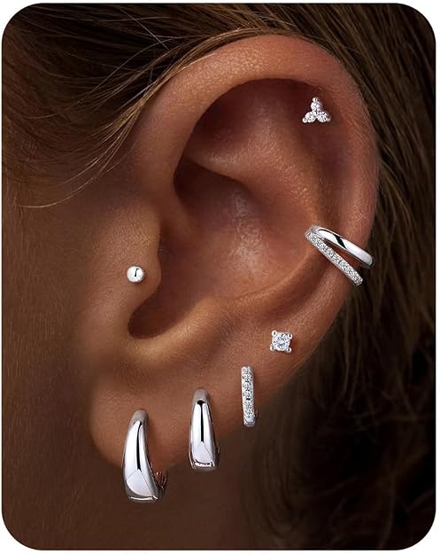 A close-up of an ear with multiple silver and diamond earrings, including hoops, studs, and a bar, adorning the earlobe, helix, and tragus.