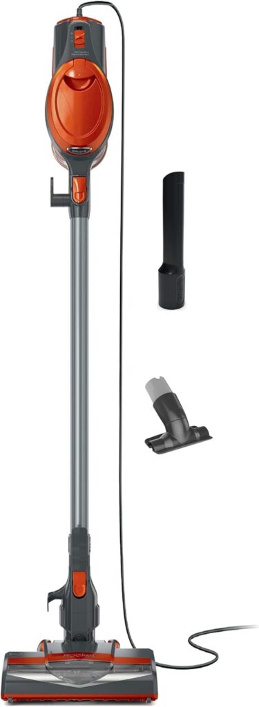 An upright orange and gray corded stick vacuum cleaner with two separate attachments: a narrow crevice tool and a small brush tool, displayed on a white background.