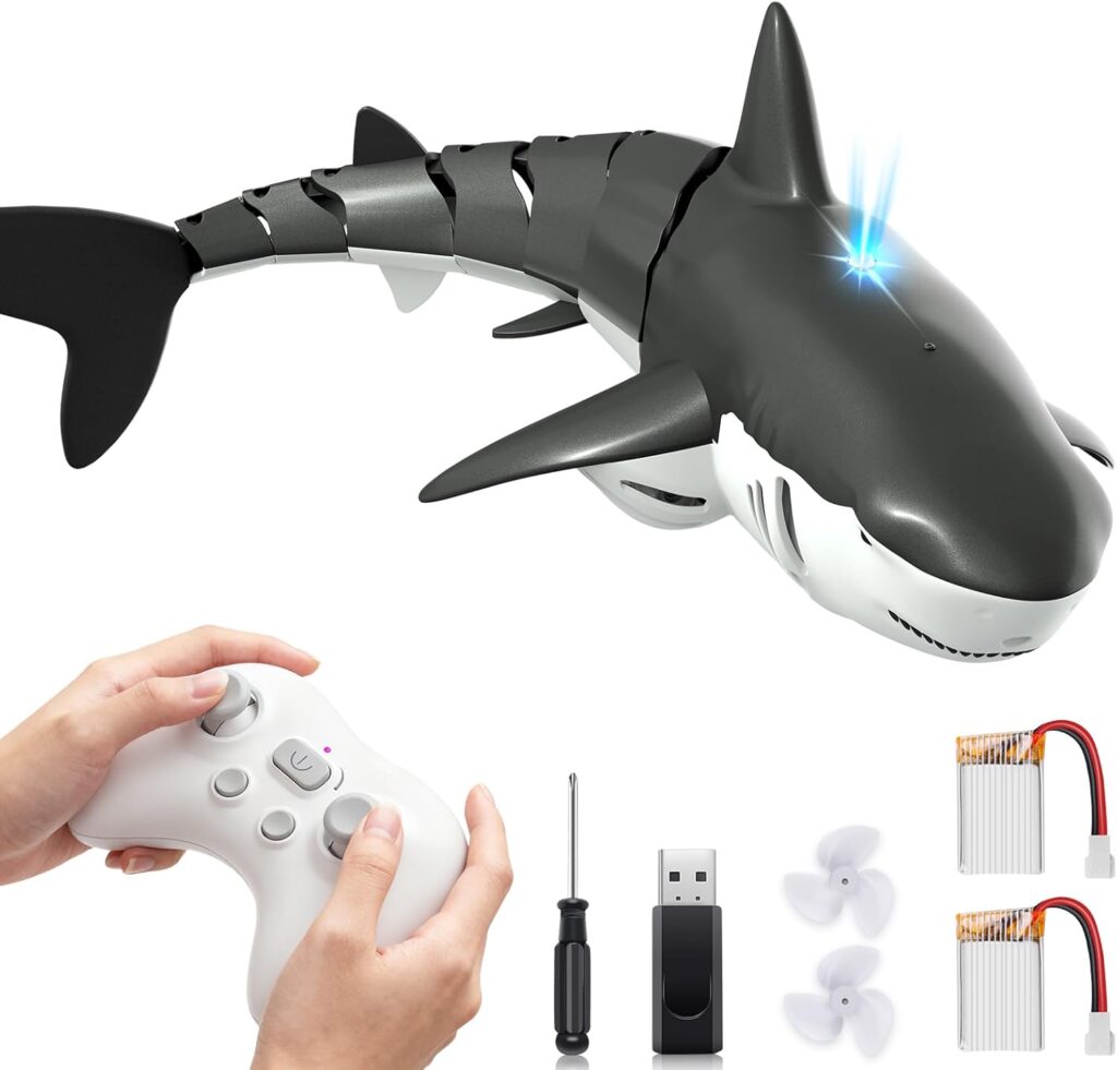 A remote-controlled robotic shark with a light on its head, shown with a white controller, screwdriver, USB charger, two propellers, and two batteries on a white background.