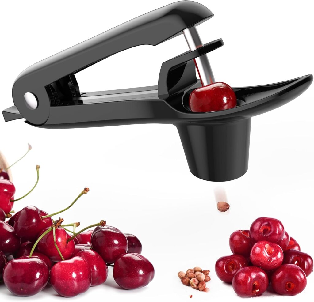 A black cherry pitter tool removing a pit from a cherry, with groups of fresh cherries and loose pits nearby on a white background.