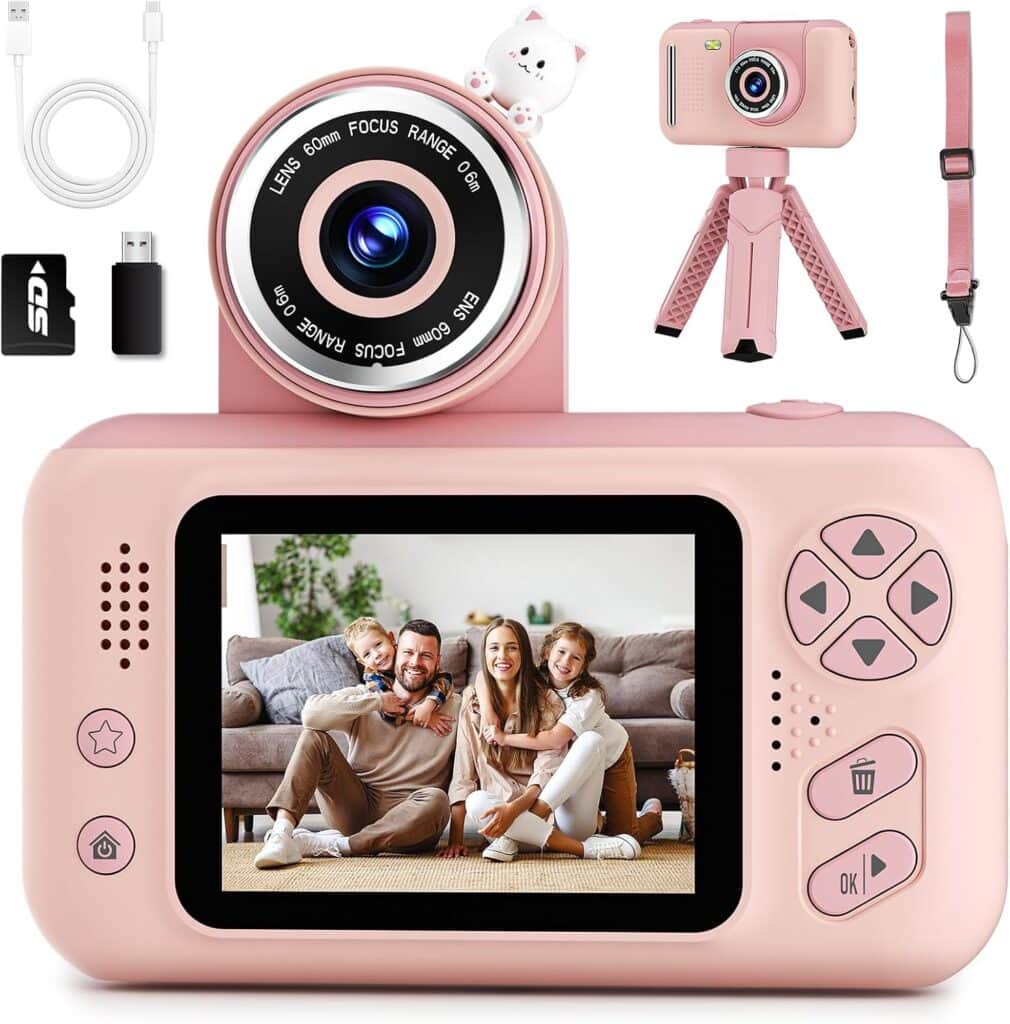 Pink digital camera kit with tripod, SD card, charging cable, and wrist strap. The camera screen displays a smiling family of four sitting together on a couch in a living room.
