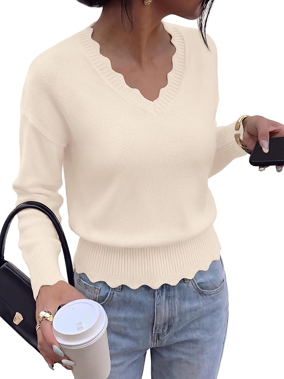 Woman wearing a cream scalloped V-neck sweater and blue jeans, holding a black purse, a coffee cup, and a smartphone against a white background.