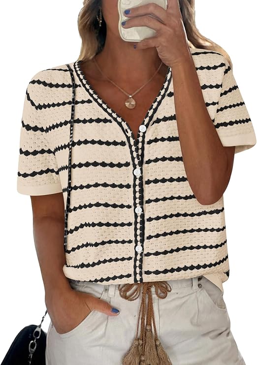 Woman taking a mirror selfie wears a cream short-sleeve crochet top with black horizontal stripes, white buttons, and light-colored shorts with a rope belt and tassels. She has a necklace and a black bag.