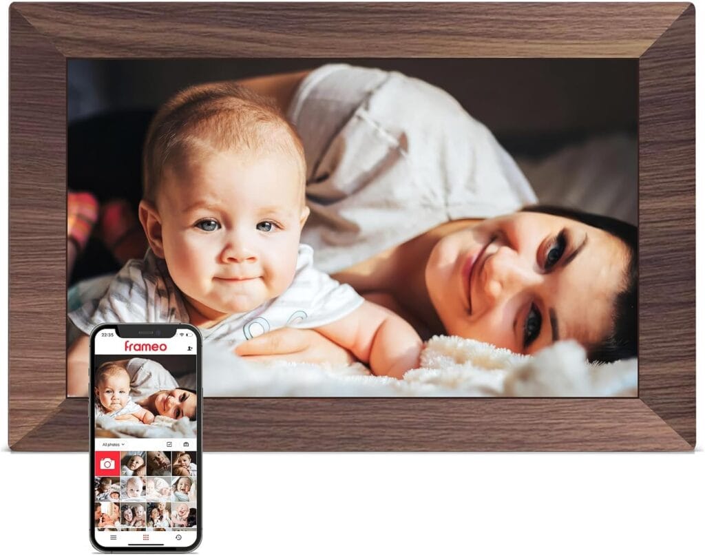 A woman and baby lying on a bed, smiling at the camera. A smartphone displaying a matching photo is shown in front of a wooden digital photo frame—perfect for capturing memories and showcasing them with this week’s Friday Deals.