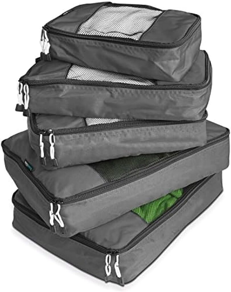 A stack of four gray packing cubes with zippers, some featuring mesh tops showing clothes inside.