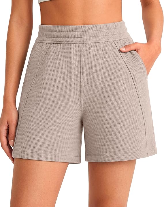 A person wearing high-waisted, light beige textured shorts with side pockets, standing with one hand in a pocket. Only the torso and upper legs are visible.