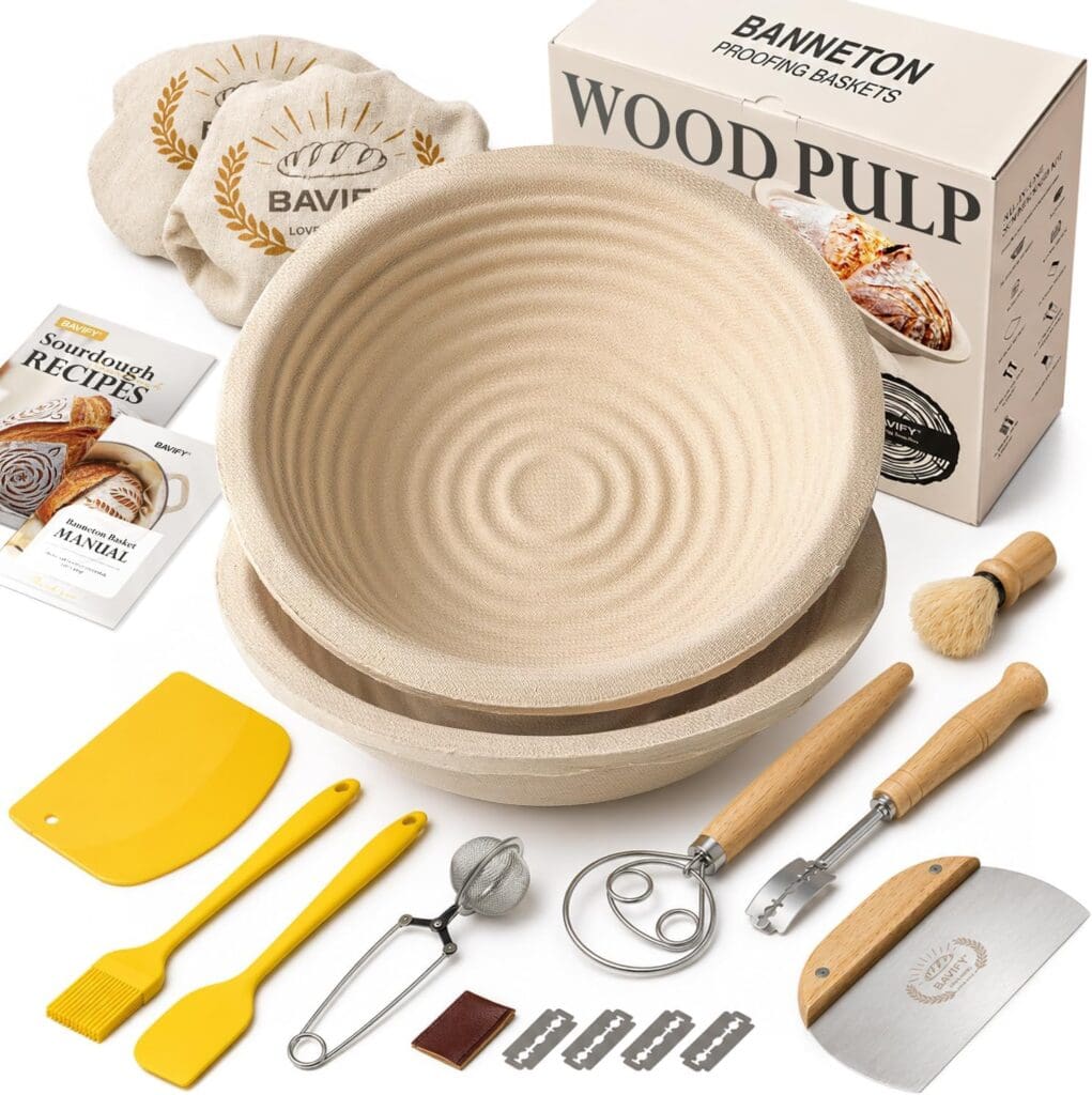 Sourdough bread baking kit with two round proofing baskets, tools like scraper, whisk, brush, scoring lame, blades, recipes booklet, cloth liner, and wood pulp packaging box displayed on a white background.