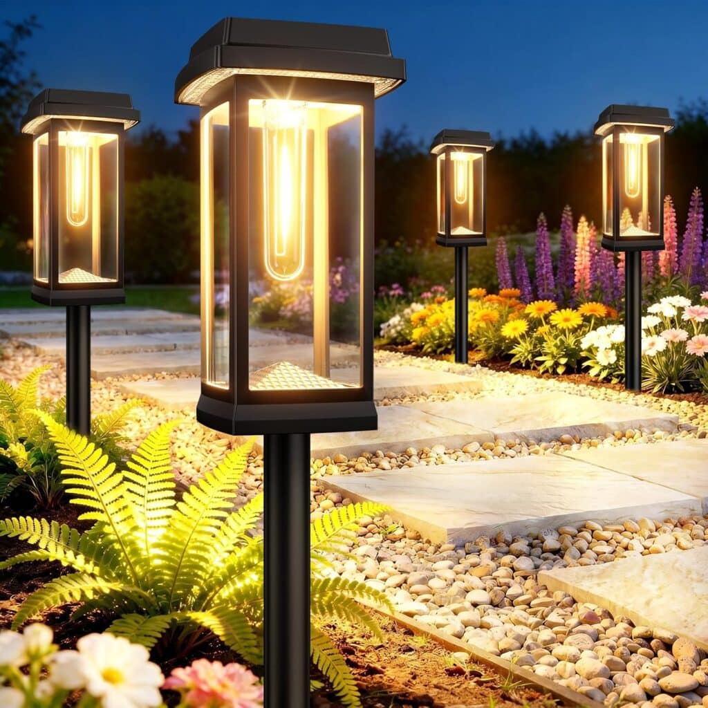 Four modern solar pathway lights illuminate a stone garden path, surrounded by colorful flowers and green ferns, at dusk.