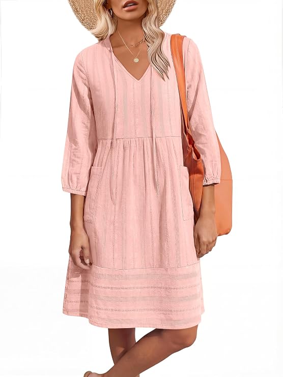 Woman in a light pink, long-sleeve, knee-length dress with pockets, wearing a straw hat and carrying an orange shoulder bag.