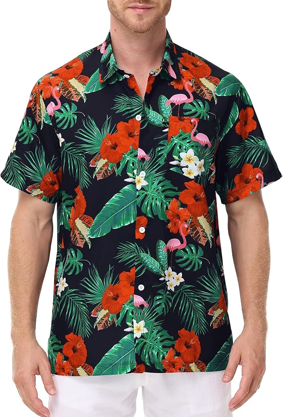 A man wearing a short-sleeve, button-up Hawaiian shirt with a tropical floral, leaf, and flamingo print in red, green, white, and pink on a black background. He has white shorts and stands against a white backdrop.