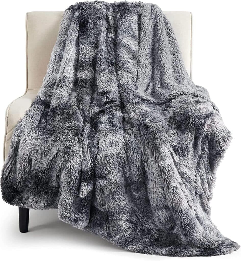 A plush, gray faux fur blanket draped over a cream-colored armchair, with the soft texture and fluffy appearance of the blanket prominently displayed.