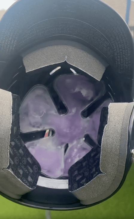The image shows the inside of a helmet with purple-colored padding or gel material, likely a cooling hat insert, visible through the helmet’s interior support structure and black padding designed to keep you cool.