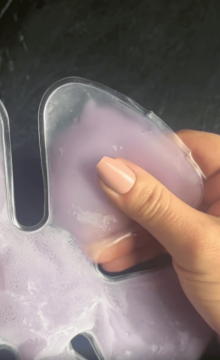 A hand with manicured nails holds a translucent plastic gel mask filled with purple gel against a dark background, perfect to Keep You Cool just like a Cooling Hat Insert.