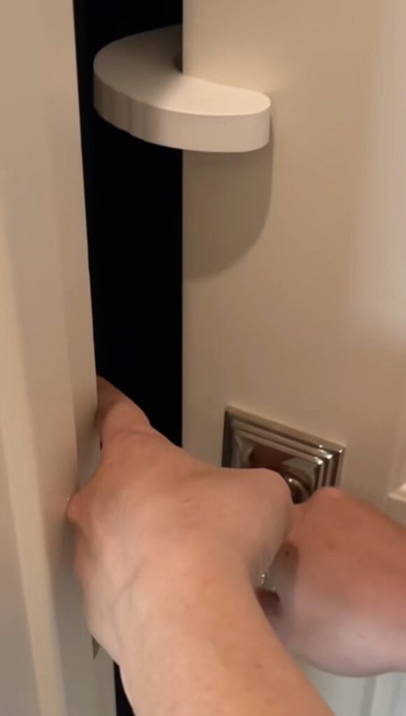 A person’s hands are shown closing a door with a white curved foam door pinch guard placed on the edge, providing extra child proofing to enhance kids safety and prevent the door from fully shutting.