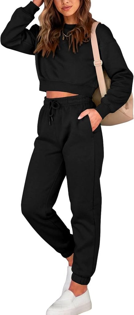 Woman wearing a black cropped sweatshirt and matching black joggers, with white slip-on sneakers and a beige shoulder bag, standing with one hand in her pocket—perfectly styled for those midweek errands or your Wednesday Deals shopping spree.