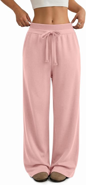 A person wearing loose, high-waisted, light pink drawstring lounge pants, a white crop top, and brown slippers. Only the lower torso and legs are visible; hands are at the sides.