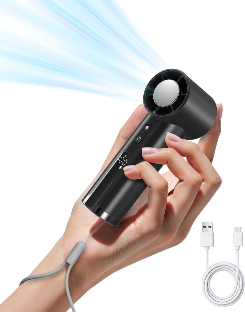 A hand holds a small black portable fan emitting blue airflow, with a gray wrist strap attached and a USB charging cable shown beside it.