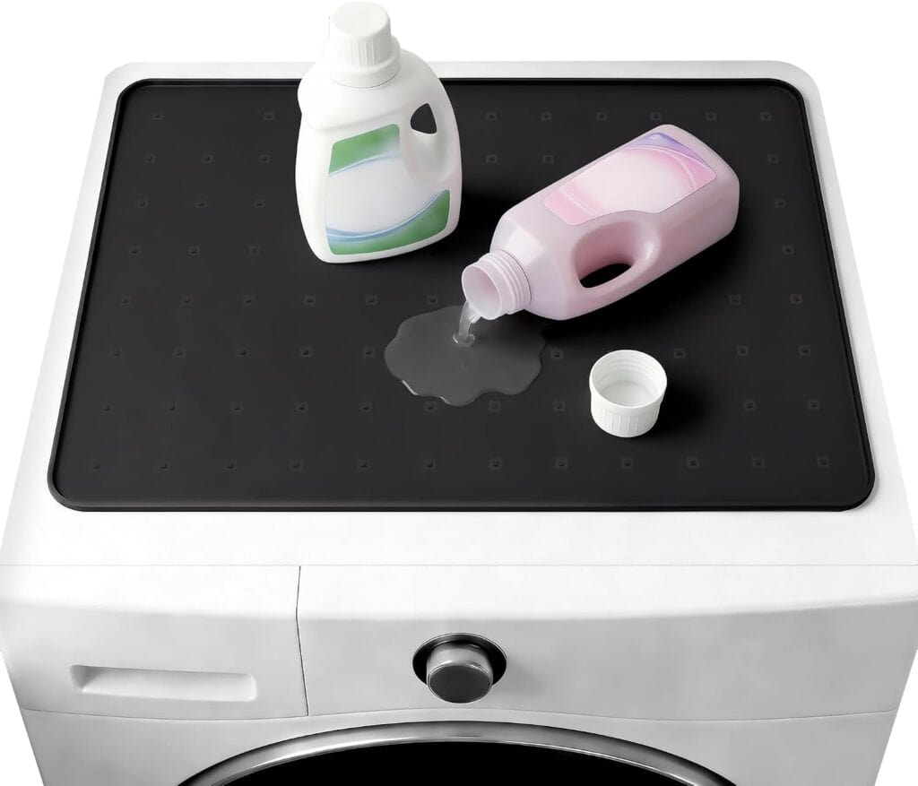 Two detergent bottles sit on top of a washing machine. One bottle is upright, the other lying down with liquid detergent spilled on a black mat. A white cap is next to the spilled bottle.