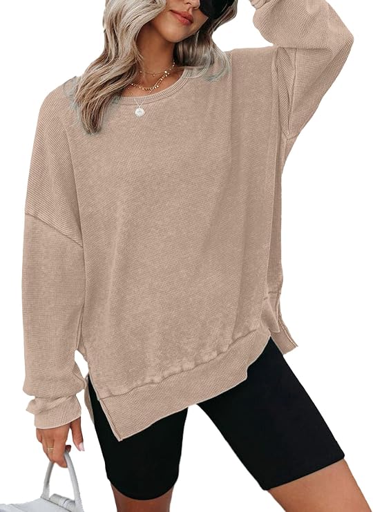 Take on the day in style with our Monday Deals: A woman wears a loose beige sweater with long sleeves and black biker shorts, holding a bag in one hand. She has wavy hair, sunglasses, and is perfectly accessorized with a necklace.