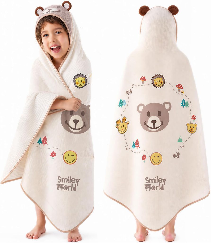 A child wears a cream-colored hooded towel with bear ears. The towel features bear and smiley face designs, colorful trees, and “Smiley World” text. The child smiles, with front and back views shown.