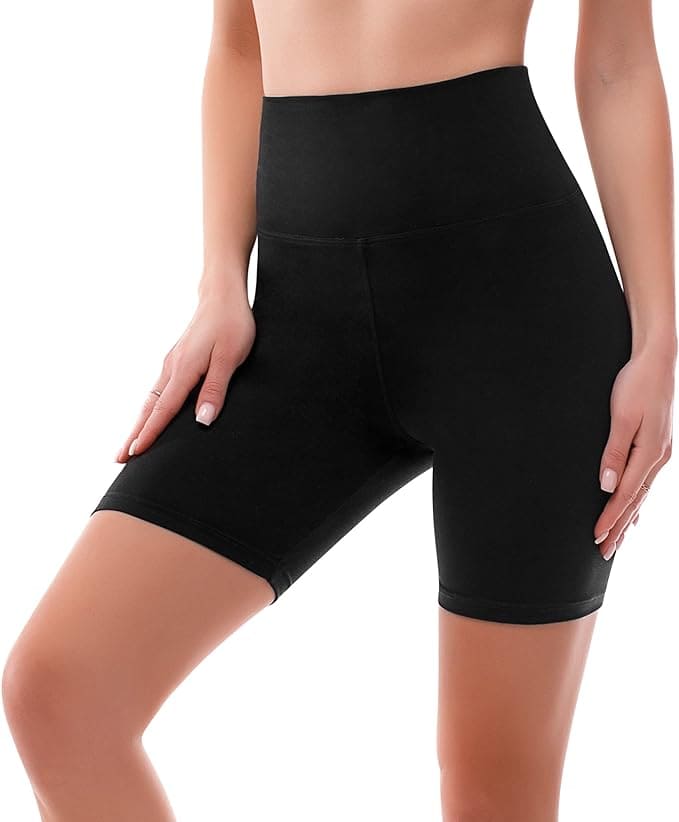 A woman wearing high-waisted, black biker shorts with her left hand resting on her left thigh and her right arm relaxed at her side, shown from midriff to mid-thigh against a white background.