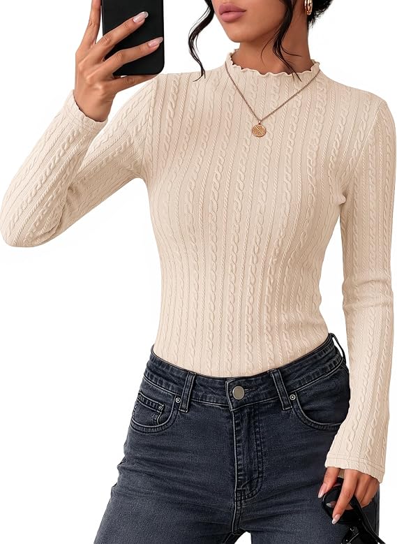 Woman wearing a cream-colored, long-sleeve, rib-knit sweater with dark jeans, a gold necklace, and earrings, taking a mirror selfie with her phone.
