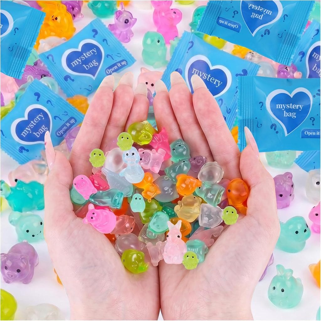 Two hands holding colorful, translucent animal-shaped figures surrounded by more similar figures and several blue “mystery bag” packages on a white surface.