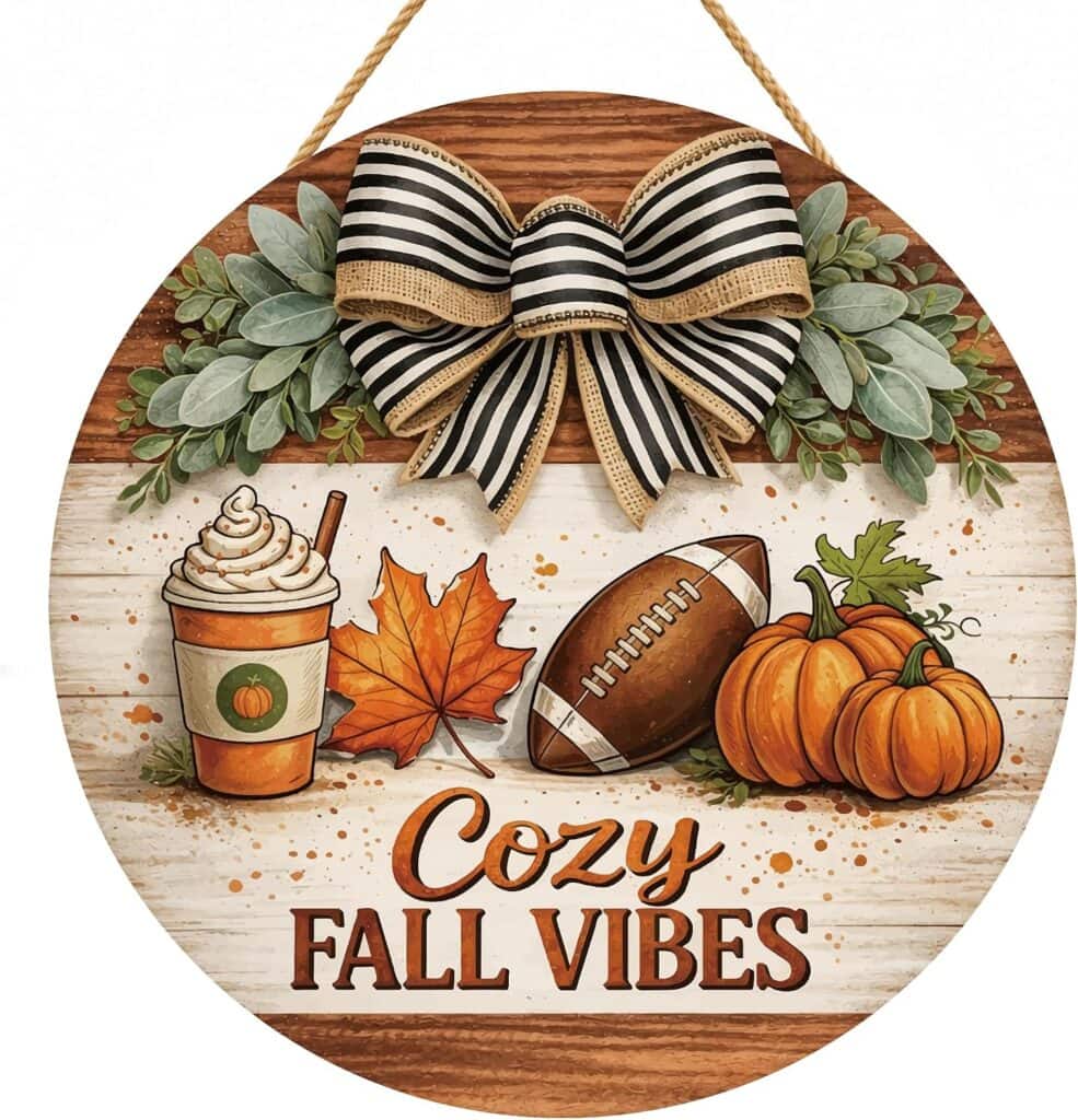 Round sign with a black and white bow, autumn leaves, pumpkins, a football, and a pumpkin drink. “Cozy Fall Vibes” is written at the bottom in bold, decorative letters.