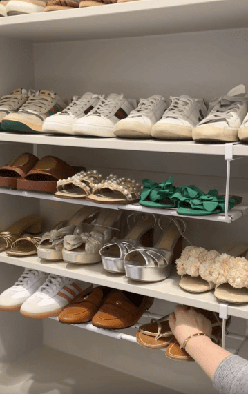 Shelves filled with neatly arranged women’s shoes, including sneakers, sandals, and heels. A hand reaches for a pair of tan sandals on the bottom shelf.