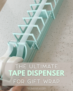 A hand pulls tape from a large, light blue tape dispenser holding two rolls, designed for gift wrapping. Text overlay reads: “The Ultimate Tape Dispenser for Gift Wrap.”.
