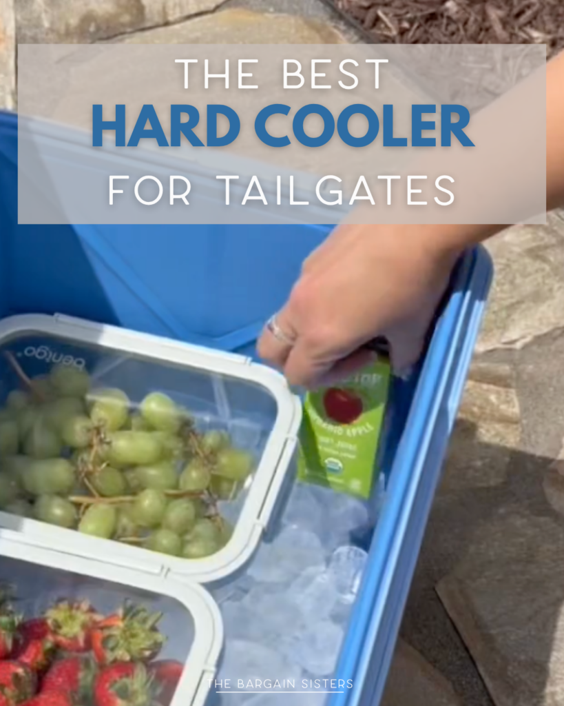 A hand places a juice box in a blue hard cooler filled with ice, grapes, and strawberries. Text reads: “The Best Hard Cooler for Tailgates.”.