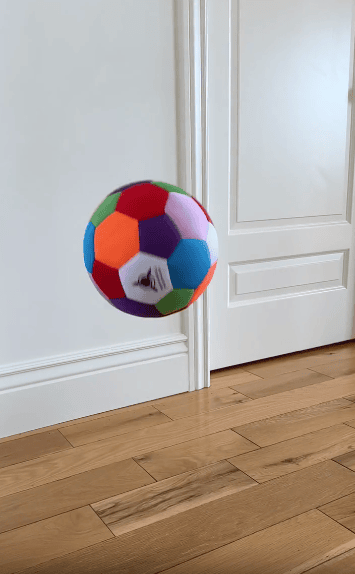 A colorful soccer ball appears to float in mid-air above a wooden floor, with a white door and white wall in the background.