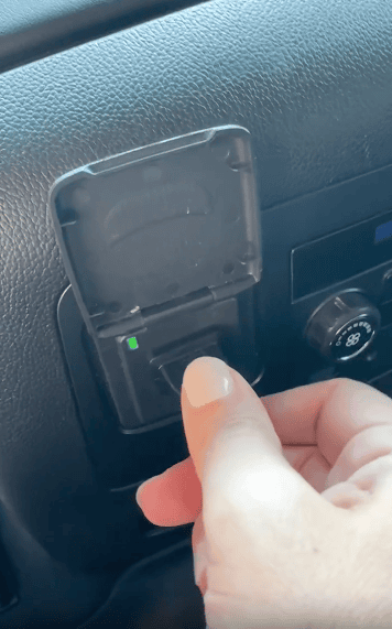 A hand flips up a small plastic cover and presses a switch on a car dashboard near the air conditioning controls.