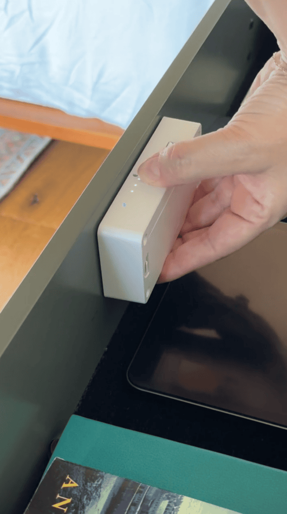 A hand installs a small rectangular device with buttons and LEDs inside a drawer above a tablet and books.