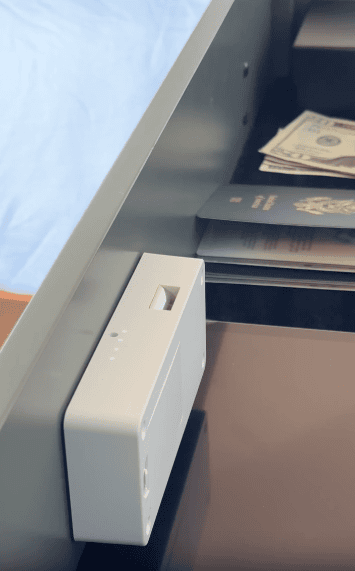 A drawer slightly open showing cash, a passport, and a white electronic device with lights and a slot inside.