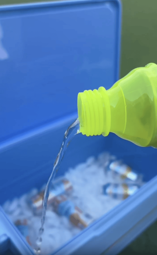 A close-up of a yellow bottle pouring liquid into a blue cooler filled with ice and canned drinks.