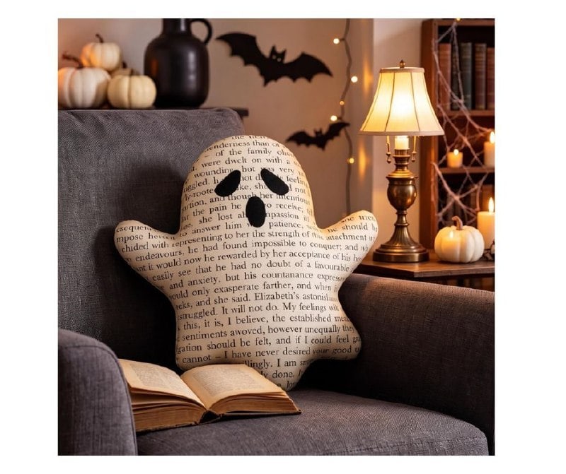 A decorative throw pillow featuring a cute ghost reading a stack of books for cozy Halloween decor featured in our Monday Deals.